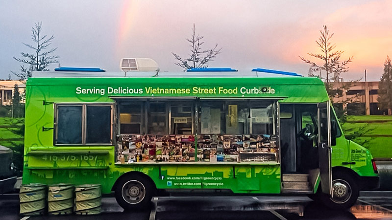 Green food truck serving delicious Vietnamese street food curbside.