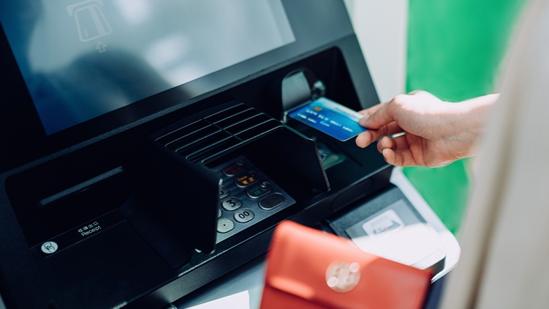 A woman holding a payment card and using an ATM